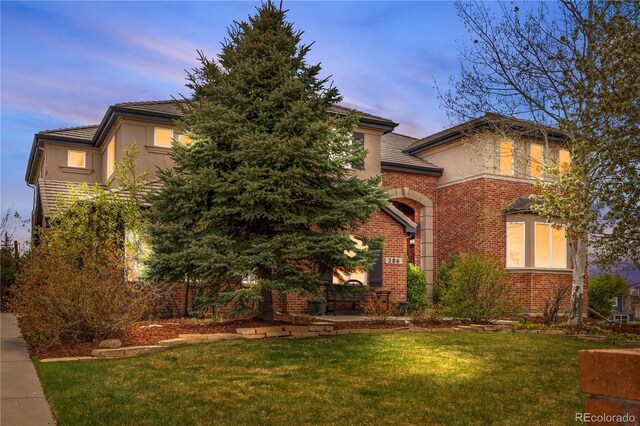 view of front facade featuring stucco siding, a front lawn, and brick siding