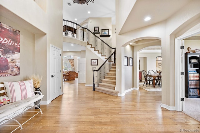 entrance foyer with stairs, arched walkways, visible vents, and light wood-style flooring