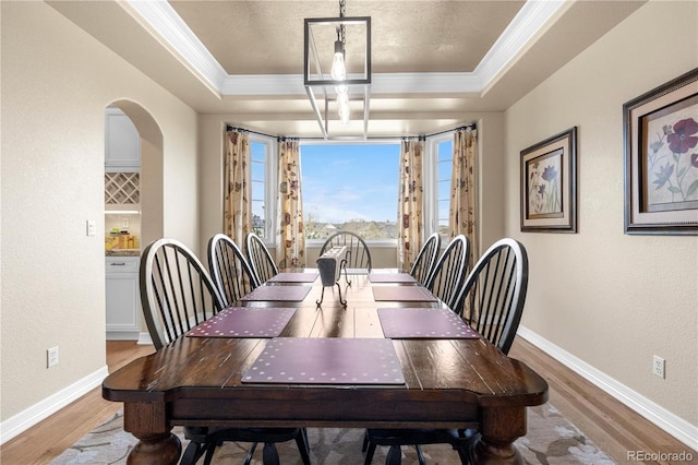 dining area with crown molding, a textured wall, wood finished floors, and a tray ceiling