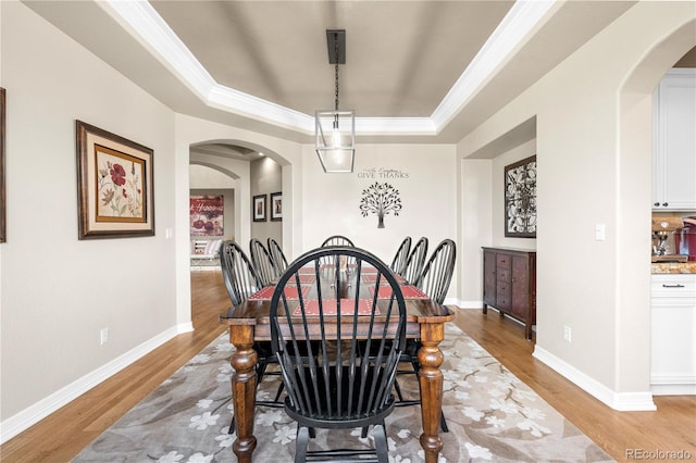 dining room featuring light wood-style floors, arched walkways, and a tray ceiling