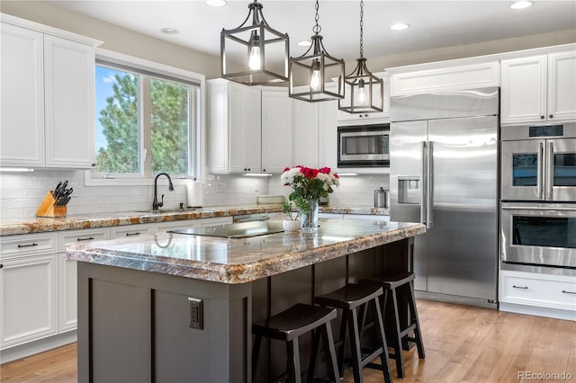 kitchen featuring a kitchen island, a sink, white cabinets, built in appliances, and recessed lighting