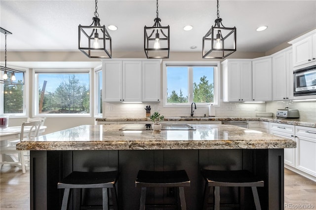 kitchen with a kitchen island, tasteful backsplash, light stone counters, light wood-style flooring, and appliances with stainless steel finishes
