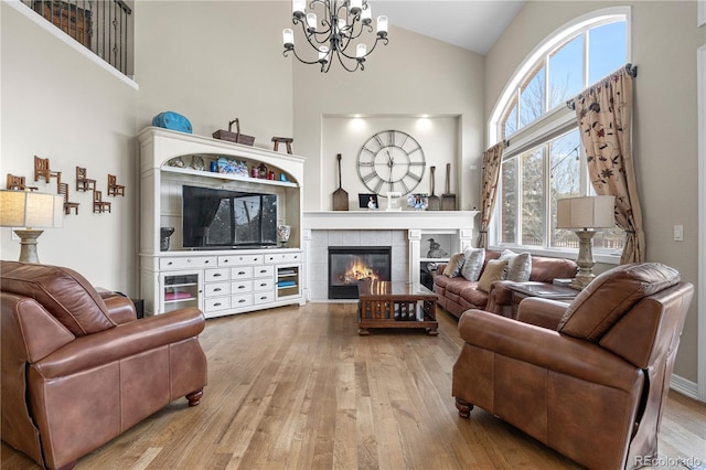 living area featuring high vaulted ceiling, an inviting chandelier, wood finished floors, and a tile fireplace