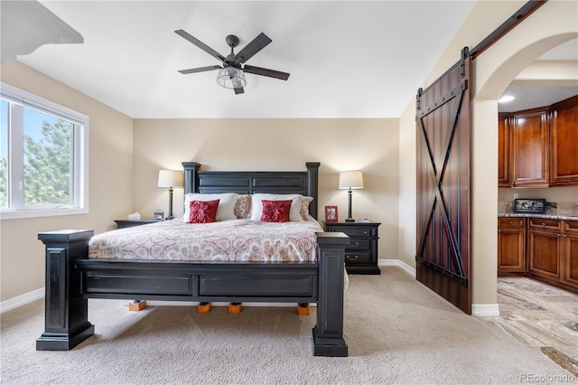 bedroom with arched walkways, baseboards, light colored carpet, and a barn door