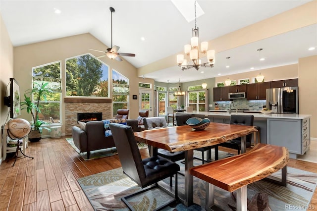 dining area featuring light wood finished floors, high vaulted ceiling, recessed lighting, a fireplace, and ceiling fan with notable chandelier