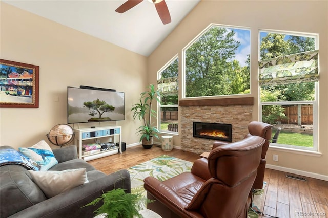 living area with a stone fireplace, vaulted ceiling, wood finished floors, and baseboards