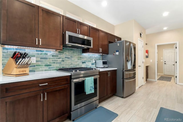 kitchen with decorative backsplash, light countertops, dark brown cabinets, and stainless steel appliances