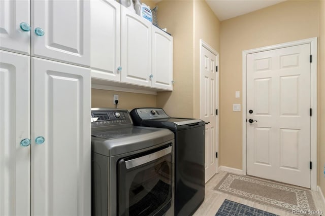 clothes washing area featuring baseboards, cabinet space, and washing machine and dryer