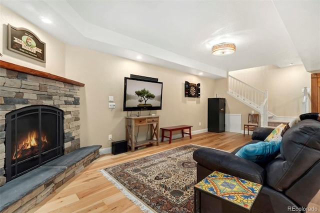 living room featuring stairway, wood finished floors, baseboards, recessed lighting, and a stone fireplace