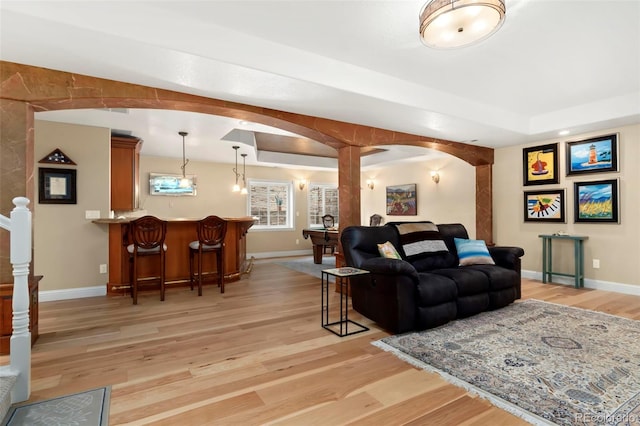 living room featuring light wood finished floors, a dry bar, baseboards, and arched walkways