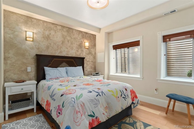 bedroom with an accent wall, wood finished floors, baseboards, and visible vents