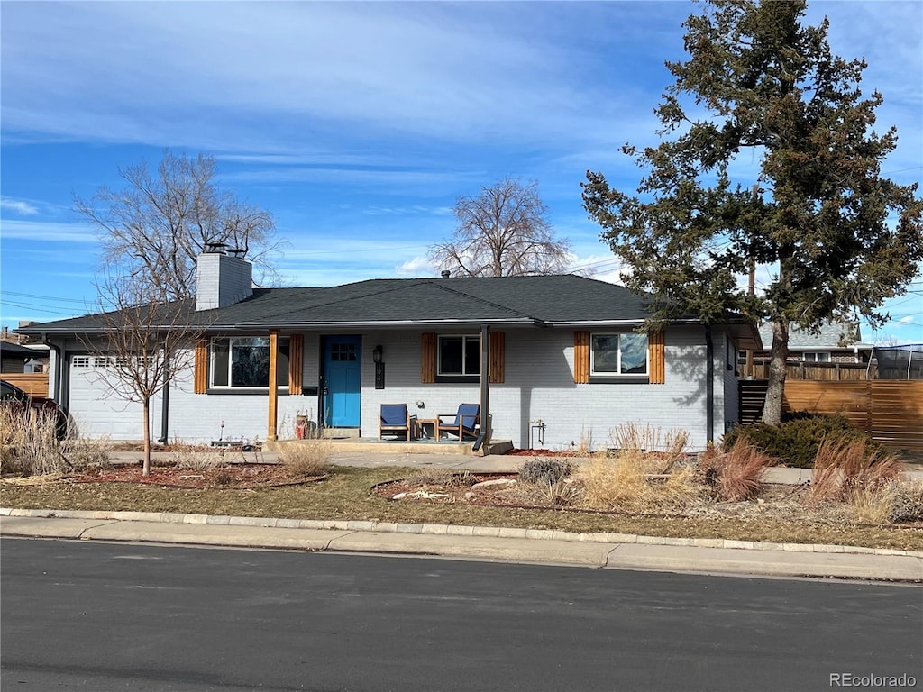 ranch-style home with a garage, covered porch, brick siding, fence, and a chimney