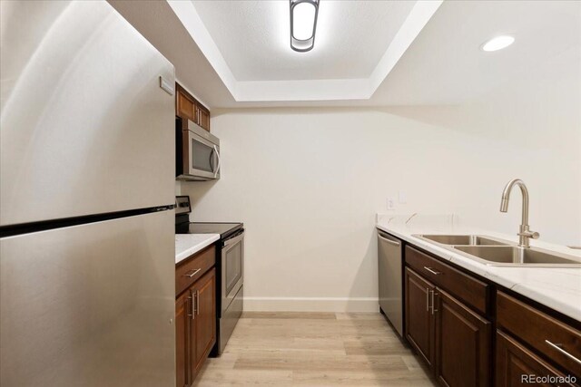 kitchen with stainless steel appliances, a sink, light wood finished floors, a tray ceiling, and light countertops