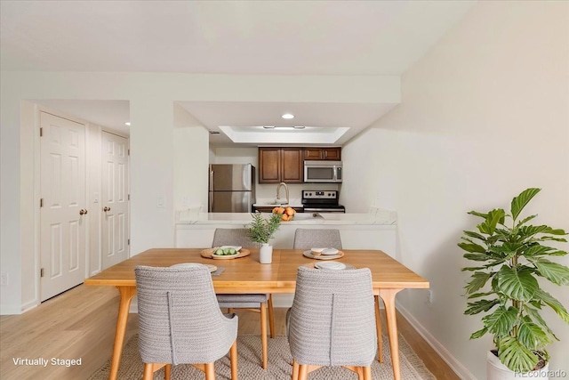 dining space featuring light wood-style floors, baseboards, recessed lighting, and a raised ceiling