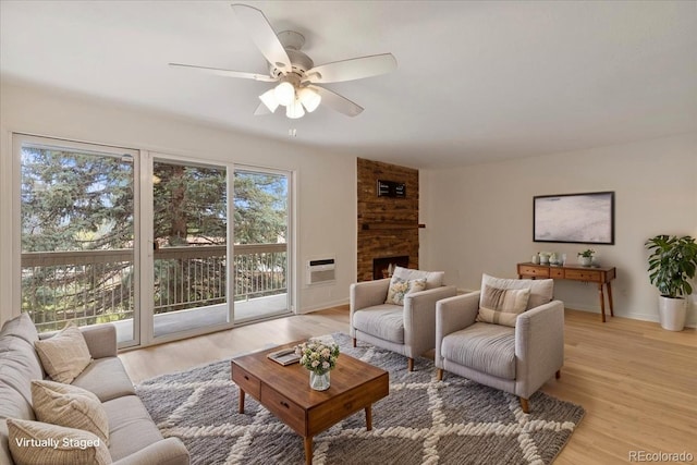 living room featuring ceiling fan, light wood-style flooring, a large fireplace, and baseboards