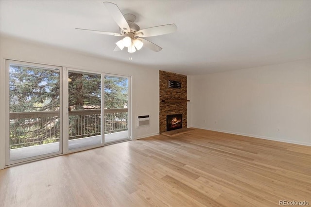 unfurnished living room with light wood-style floors, ceiling fan, a fireplace, baseboards, and a wall unit AC