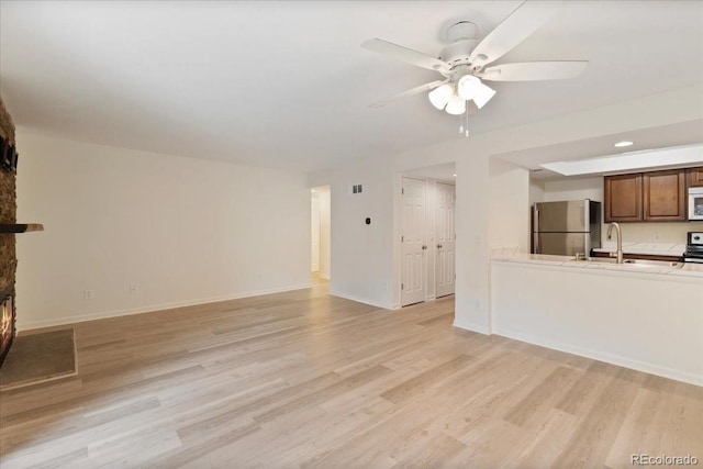 unfurnished living room with ceiling fan, light wood-style floors, a fireplace, and a sink