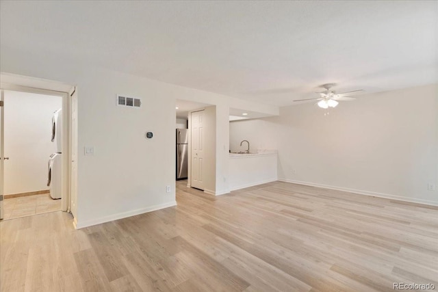 unfurnished living room featuring ceiling fan, stacked washer / dryer, light wood finished floors, baseboards, and recessed lighting