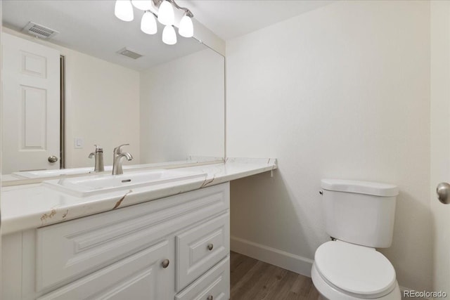 half bathroom with baseboards, wood finished floors, vanity, toilet, and a chandelier