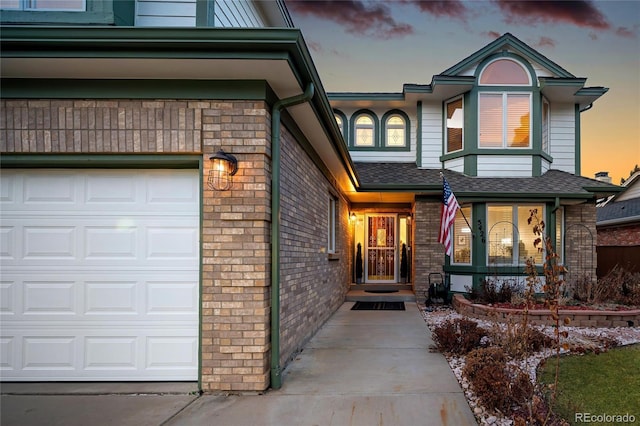 view of exterior entry featuring a garage, brick siding, and roof with shingles