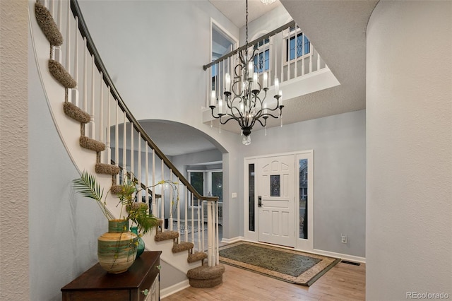 entrance foyer featuring a chandelier, stairs, a high ceiling, wood finished floors, and arched walkways