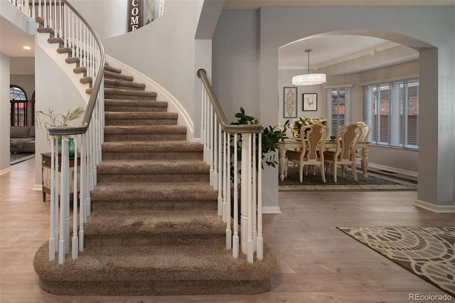 stairs featuring wood finished floors, baseboards, a high ceiling, arched walkways, and crown molding