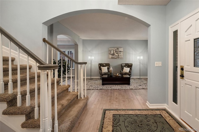 foyer featuring hardwood / wood-style floors, stairway, baseboards, and arched walkways