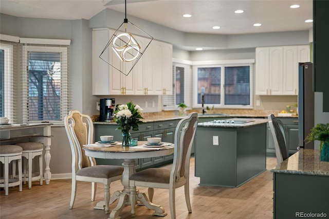 kitchen featuring light stone countertops, freestanding refrigerator, hanging light fixtures, white cabinets, and light wood-style floors