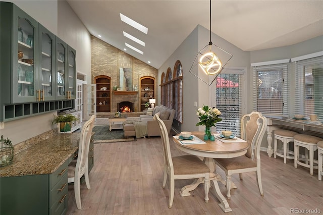 dining space featuring a chandelier, a brick fireplace, a skylight, and light wood-style floors