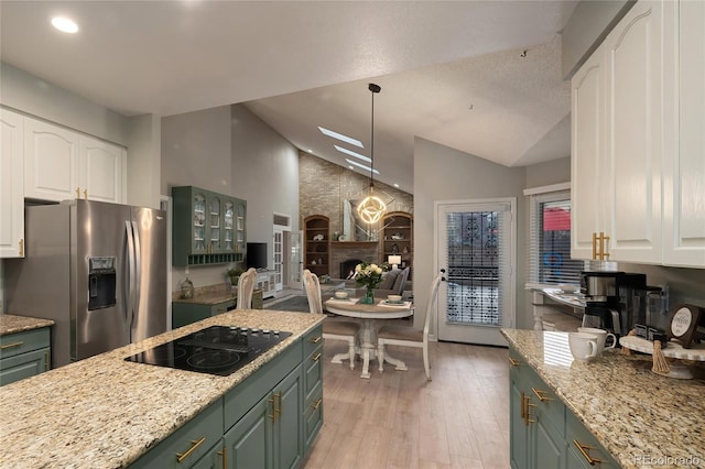 kitchen with a fireplace, stainless steel fridge with ice dispenser, vaulted ceiling, white cabinets, and black electric cooktop