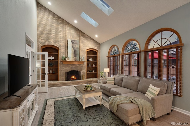 living area with a skylight, built in features, a fireplace, and light wood-type flooring