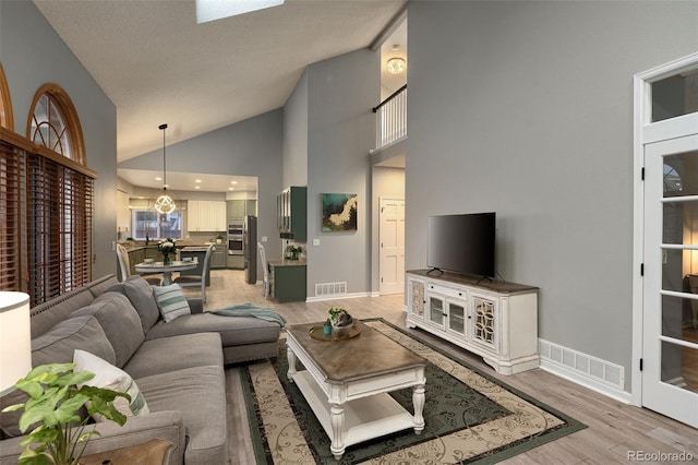 living area featuring baseboards, visible vents, light wood finished floors, and high vaulted ceiling