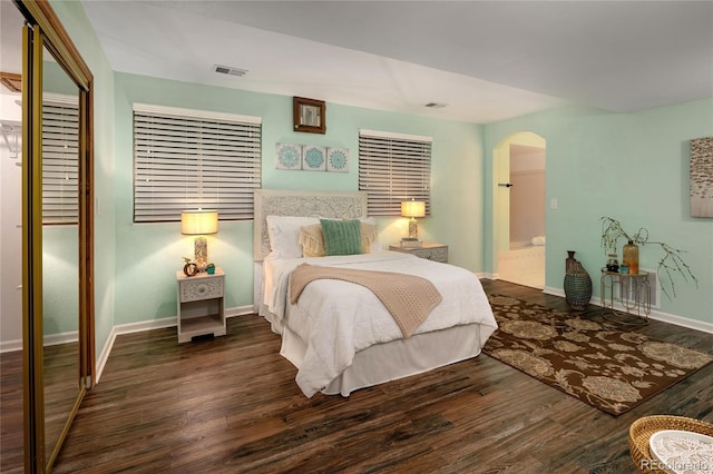 bedroom featuring wood finished floors, baseboards, visible vents, arched walkways, and a closet