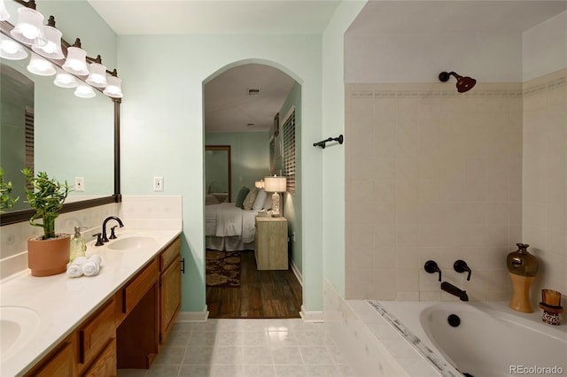 ensuite bathroom featuring ensuite bathroom, a sink, tile patterned flooring, double vanity, and a relaxing tiled tub