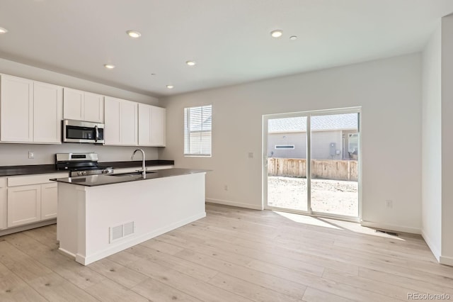 kitchen with dark countertops, appliances with stainless steel finishes, a sink, light wood-style floors, and visible vents