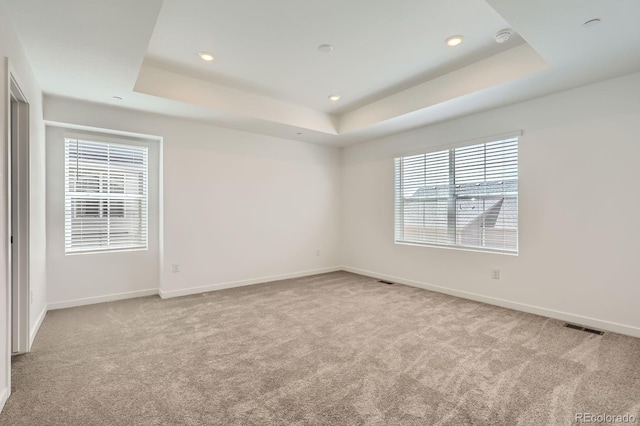 empty room with visible vents, a raised ceiling, carpet floors, and baseboards