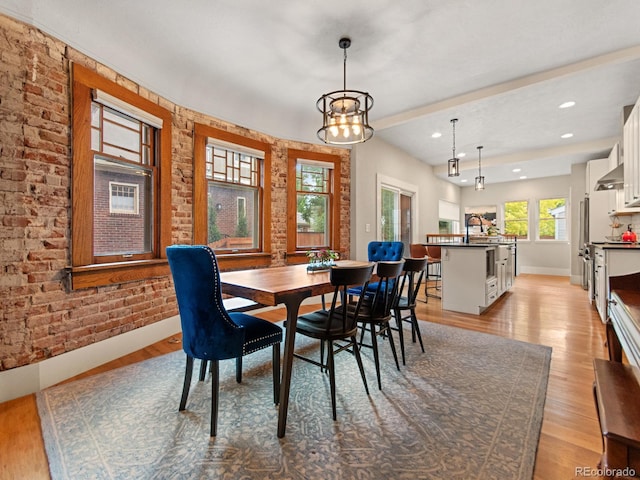 dining area featuring a chandelier, light hardwood / wood-style flooring, brick wall, and sink