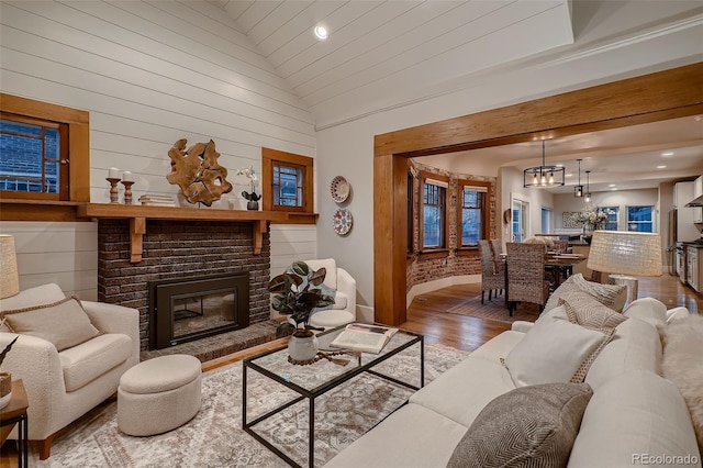 living room with wood-type flooring, an inviting chandelier, high vaulted ceiling, and a brick fireplace