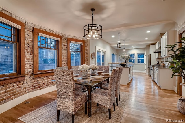 dining area featuring a chandelier, sink, brick wall, and light hardwood / wood-style flooring