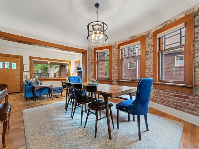 dining room featuring a notable chandelier, brick wall, and light hardwood / wood-style flooring