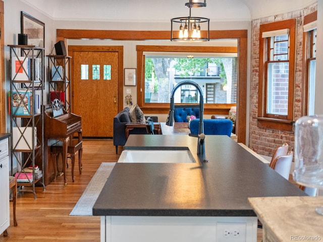 dining space featuring a chandelier, sink, light hardwood / wood-style floors, and brick wall