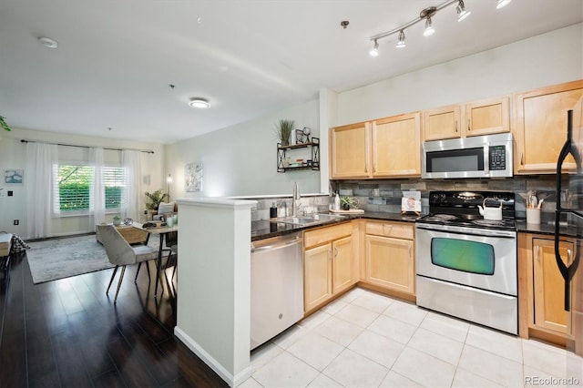 2895 W Riverwalk Cir Unit 104, Littleton, CO 80123 - kitchen featuring stainless steel appliances, light brown cabinetry, dark countertops, a peninsula, and backsplash