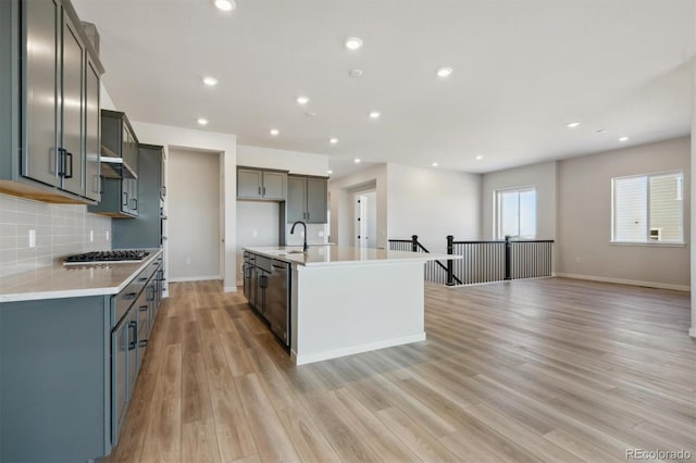 kitchen featuring stainless steel appliances, light countertops, decorative backsplash, a sink, and light wood-type flooring