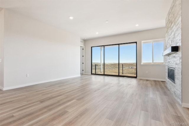 unfurnished living room featuring recessed lighting, baseboards, a fireplace, and light wood finished floors