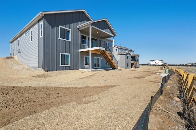 rear view of house featuring board and batten siding, fence, a balcony, and dirt driveway