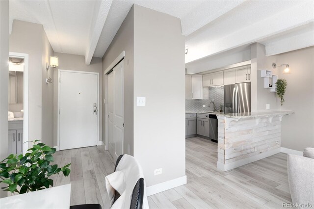 555 E 10th Ave Unit 206, Denver, CO 80203 - kitchen with appliances with stainless steel finishes, light wood-style flooring, backsplash, a peninsula, and gray cabinets