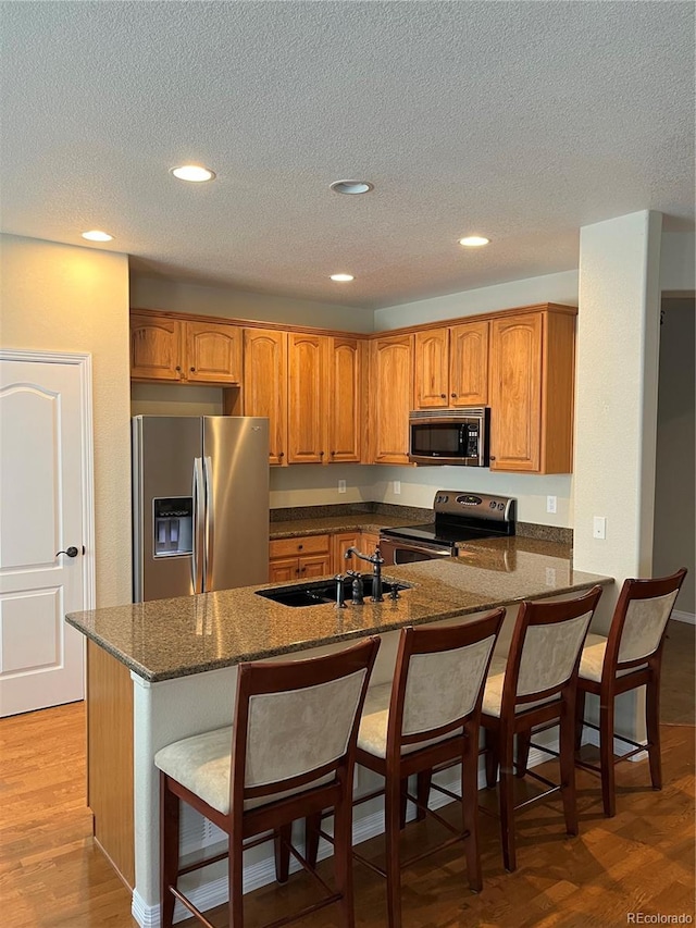 kitchen featuring sink, a kitchen breakfast bar, kitchen peninsula, appliances with stainless steel finishes, and light wood-type flooring