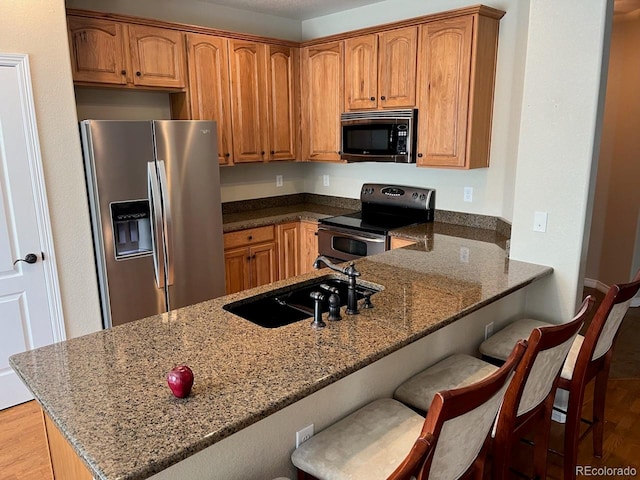 kitchen with kitchen peninsula, a kitchen bar, dark stone counters, stainless steel appliances, and sink