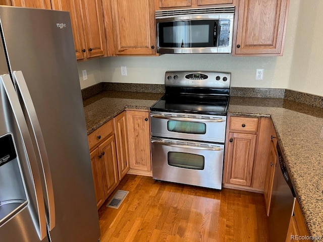 kitchen featuring light hardwood / wood-style floors, dark stone countertops, and appliances with stainless steel finishes