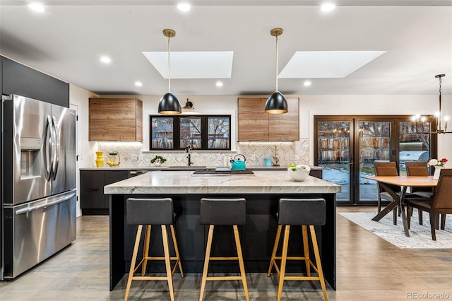 kitchen with stainless steel refrigerator with ice dispenser, a skylight, a center island, a sink, and a kitchen bar